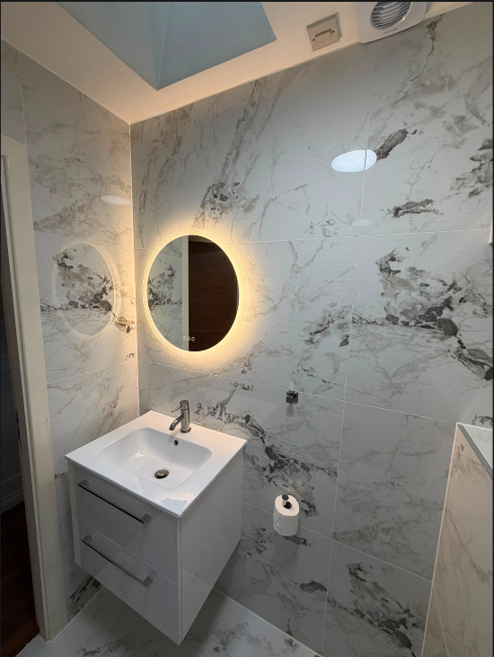 Close-up of a luxury marble bathroom with backlit round mirror and floating vanity